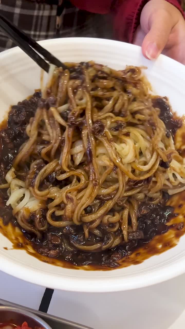Una persona usa le bacchette per mescolare una saporita salsa di fagioli neri nei noodles in una ciotola.