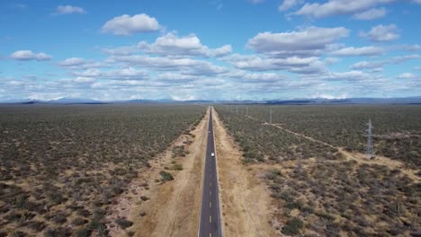 Un-Camino-Recto-Con-Un-Auto-Blanco-Que-Atraviesa-El-Vasto-Desierto-De-Baja-California-Sur,-Vista-Aérea