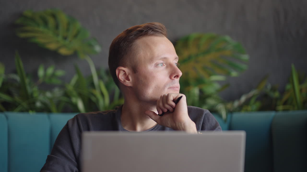 Thoughtful 30s man thinking of problem solution working on laptop. Serious doubtful male professional looking away at laptop considering market risks making difficult decision sitting at desk