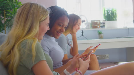 Grupo-De-Amigas-Adolescentes-Multiculturales-Con-Teléfonos-Móviles-Colgando-En-El-Dormitorio-En-Casa