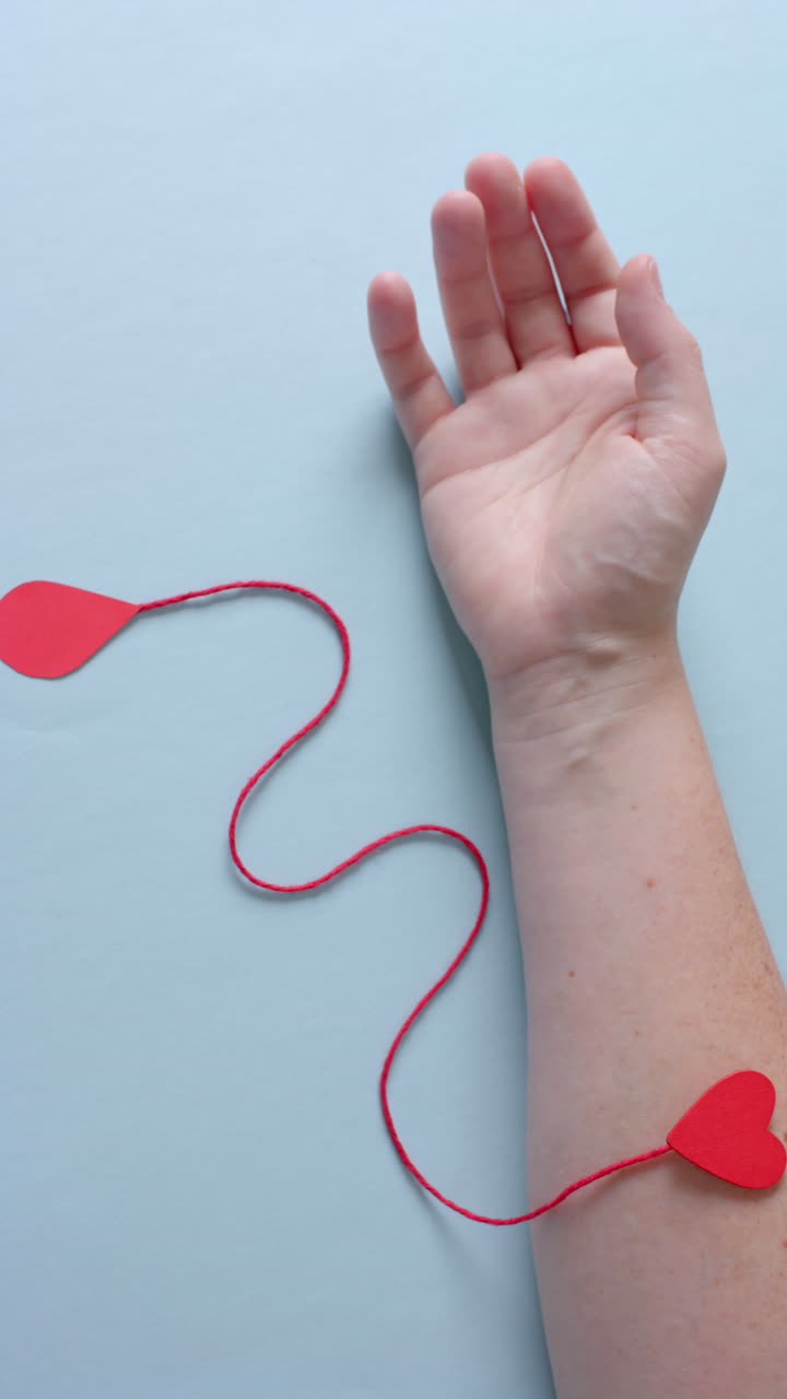 Video verticale della mano di un uomo caucasico con una goccia di sangue, un filo rosso e un cuore, al rallentatore.