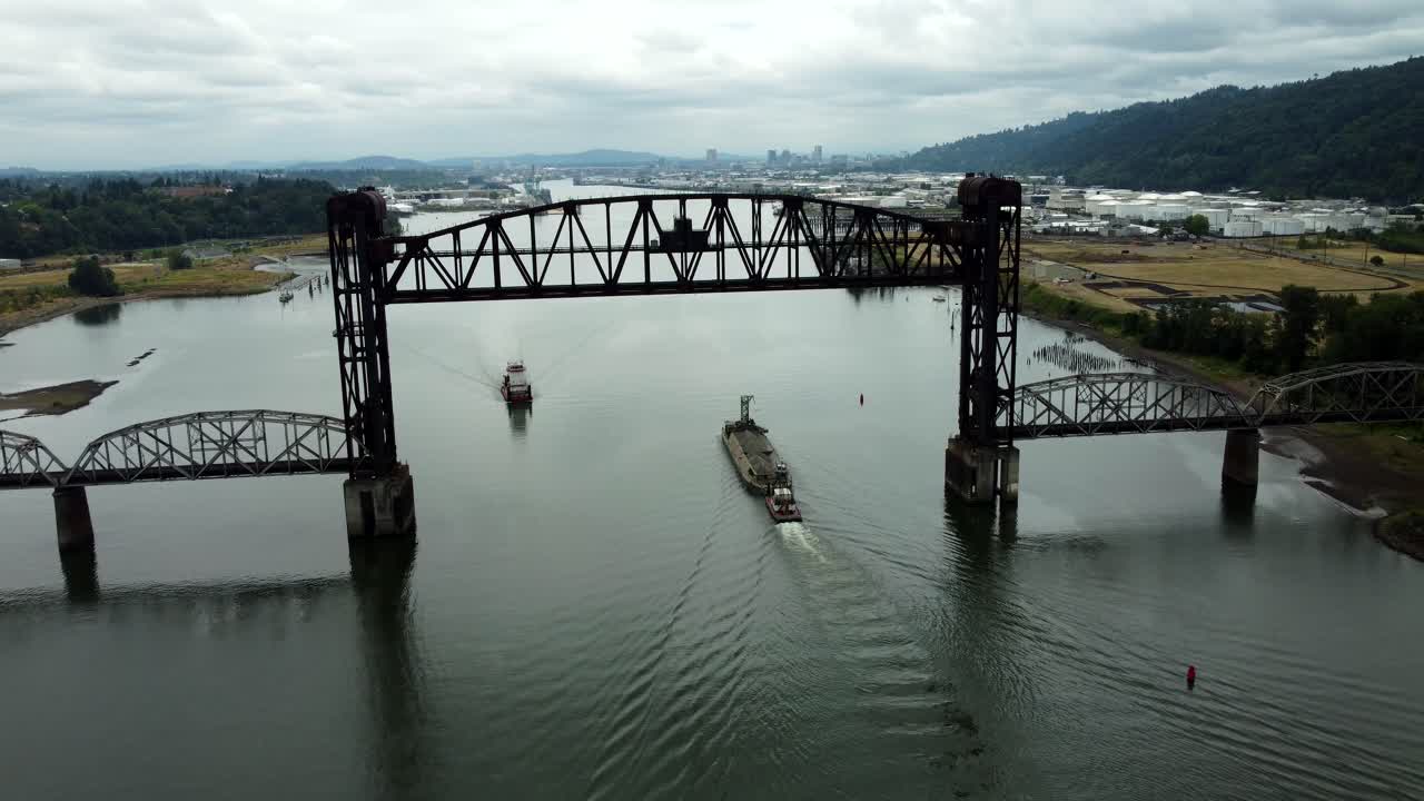 US, Oregon, Portland, St Johns, 2025-07-26 - Drone view of a barge being pushed by a tug on the Willamette River under the raised railroad bridge