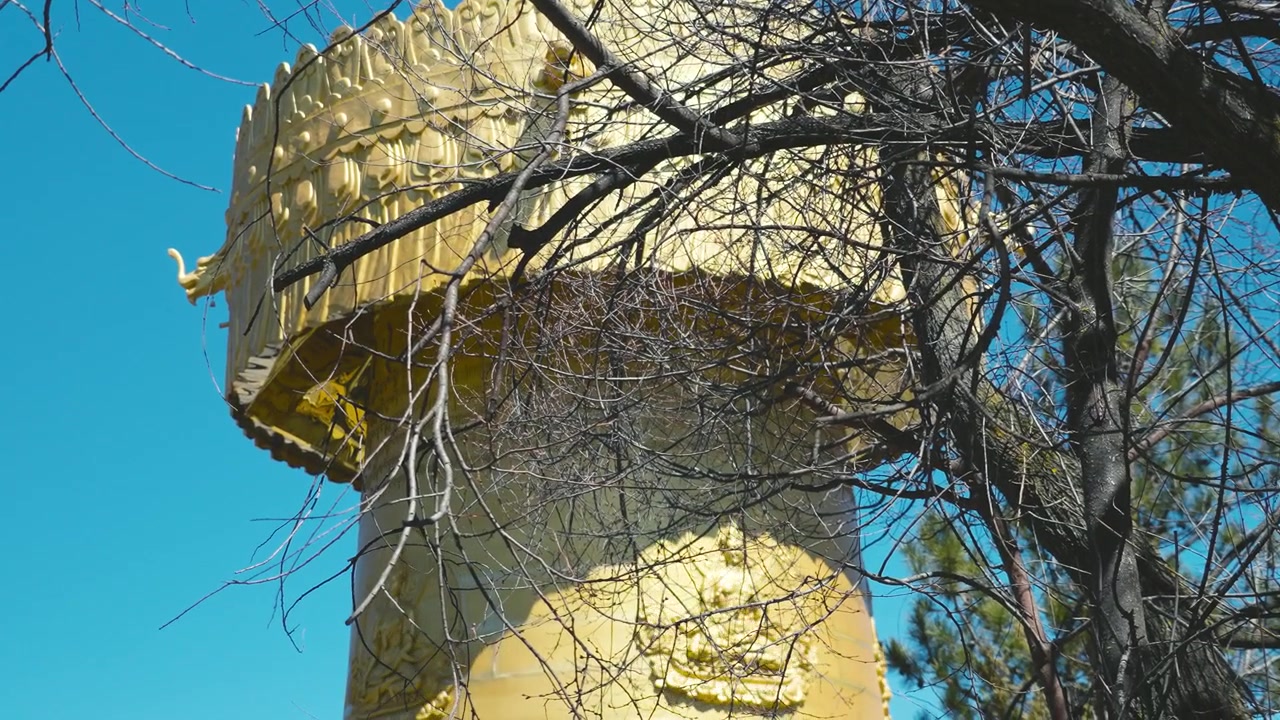Una magnifica stupa dorata nella città di Shangri-La fa capolino tra i rami spogli invernali sotto un cielo blu vibrante, fondendo spiritualità con bellezza naturale.
