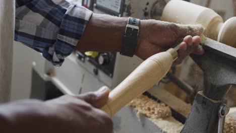 Close-up-of-african-american-male-carpenter-hand's-turning-wood-on-a-lathe-at-carpentry-shop