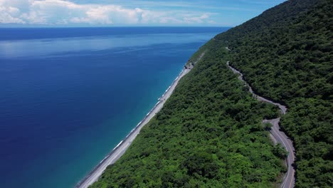 Flying-along-a-narrow-cliff-side-highway-overlooking-a-secluded-tropical-beach-in-Eastern-Taiwan