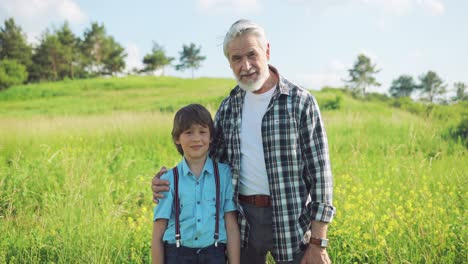 portrait of a senior man hugging to his grandson in the park and looking at camera on a sunny day