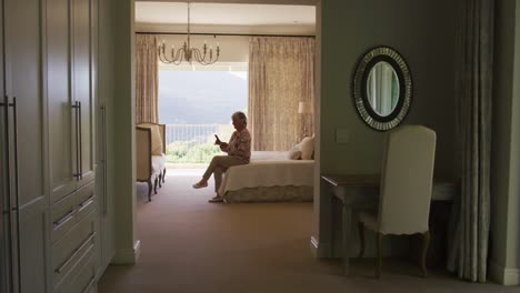 caucasian senior woman using smartphone while sitting on the bed at home