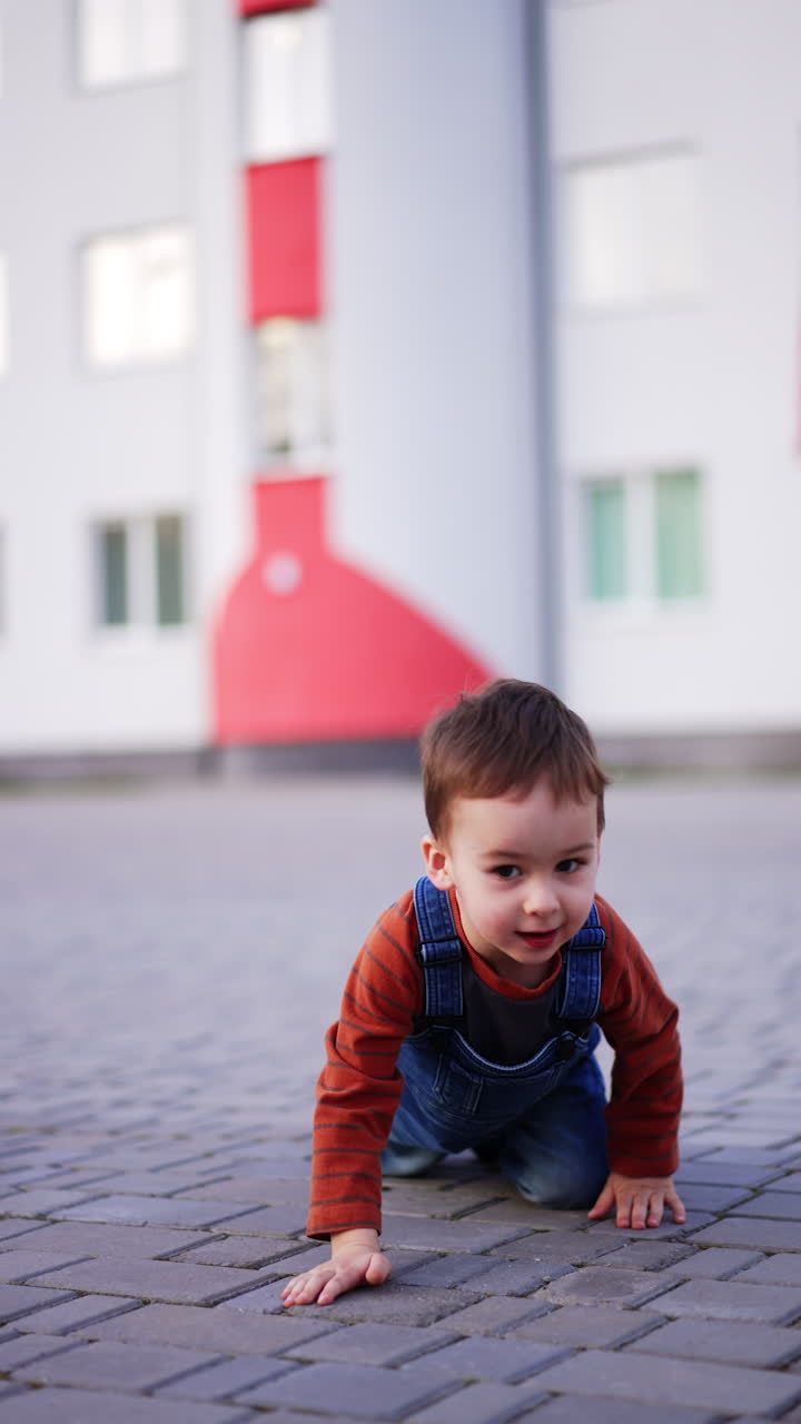Baby boy approaches the camera crawling by the paved road. Funny kid on the walk outdoors. Vertical video.