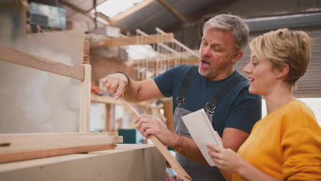 Female-Apprentice-Making-Notes-Learning-From-Mature-Male-Carpenter-In-Furniture-Workshop