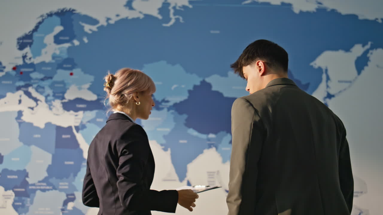 Analysts discussing world map in monitoring office back view. Employees working