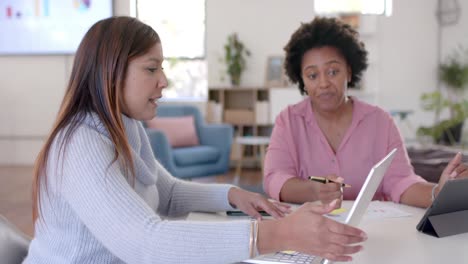 diverse business female colleagues in discussion using tablet and laptop in office, slow motion