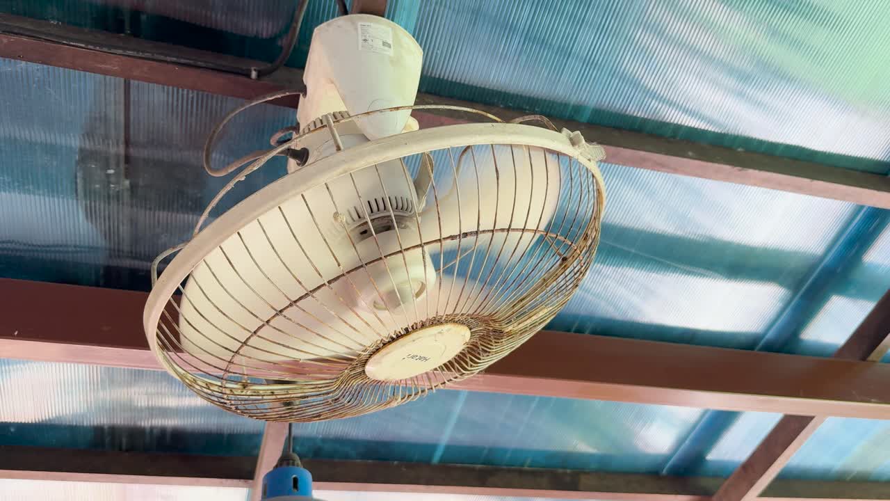 A rusty ceiling fan spins under a translucent roof at a clifftop restaurant in Phuket, Thailand, creating a relaxed, tropical atmosphere