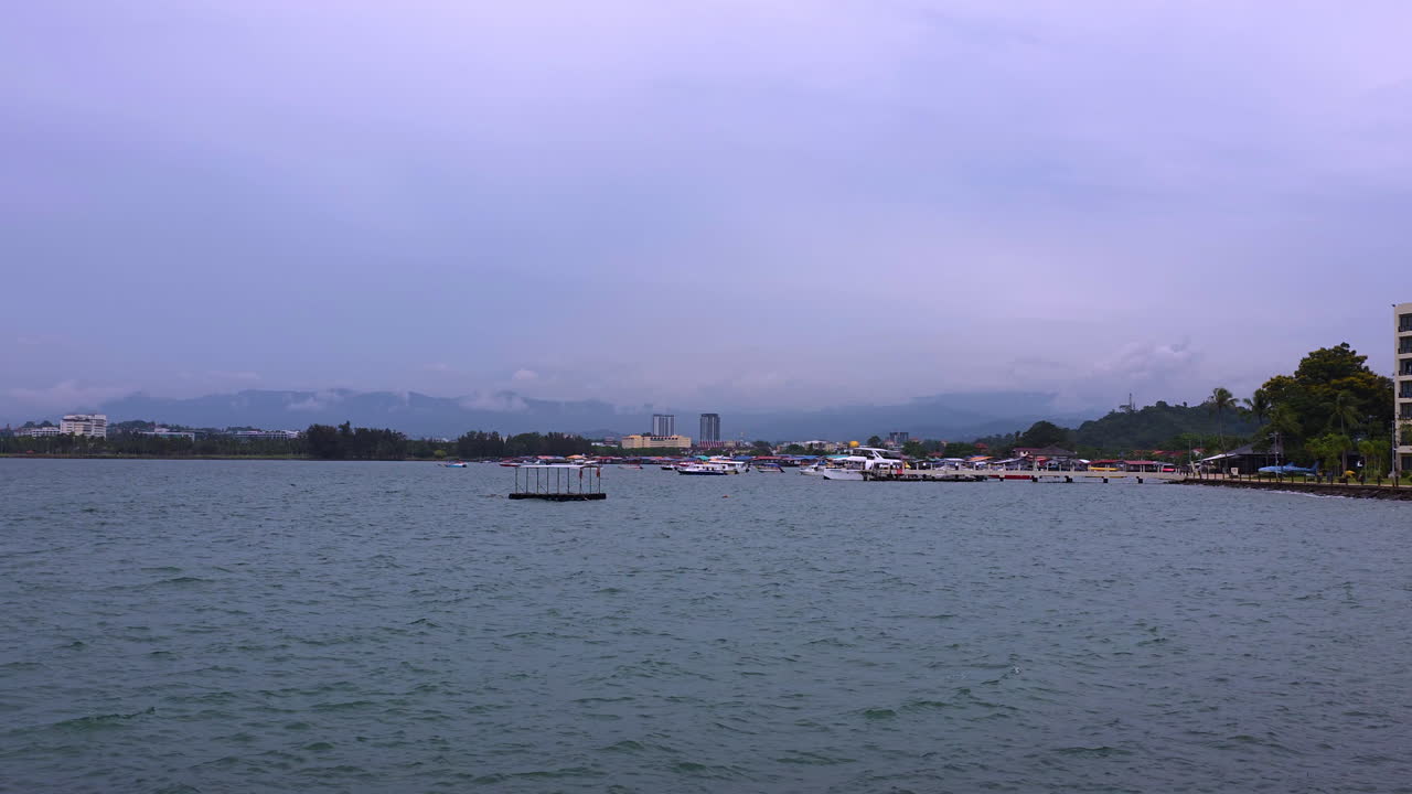 Coastal view from Shangri-La Tanjung Aru Resort in Kota Kinabalu, showing calm harbor waters, docked boats, distant city skyline, and mountain backdrop under a soft cloudy sky