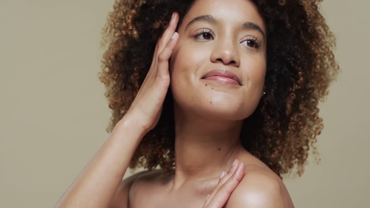 Mulher birracial feliz com cabelo cacheado escuro em fundo bege, em câmera lenta.