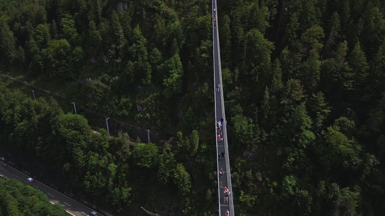 Aerial view of the world's longest pedestrian suspension bridge, connecting Ehrenberg Castle and Fort Claudia in Austria, over a busy road and surrounded by a forest of trees
