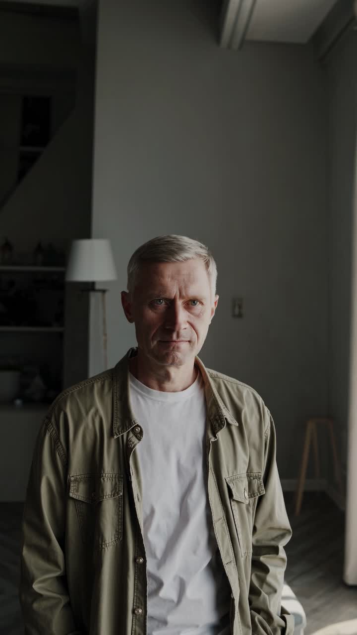 retrato de un hombre maduro confiado con cabello gris y chaqueta verde de pie en un apartamento moderno, mirando serio y reflexivo, con una expresión serena en su cara