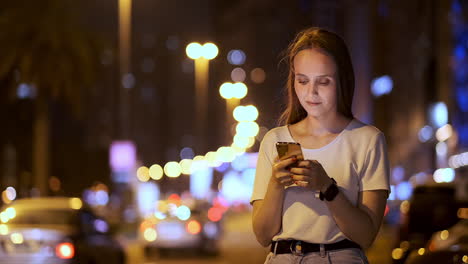 young woman tourist travels through the night megalopolis and writes text messages on social networks about the journey holds the phone in her hands and looks at the screen of the gadget