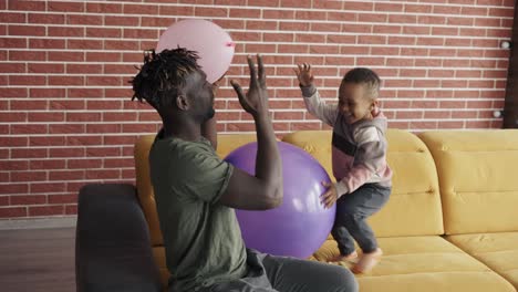 african-american father playing with cute little boy using two balloons