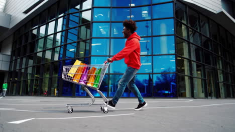 happy man runs energetically with shopping cart full of colorful bags