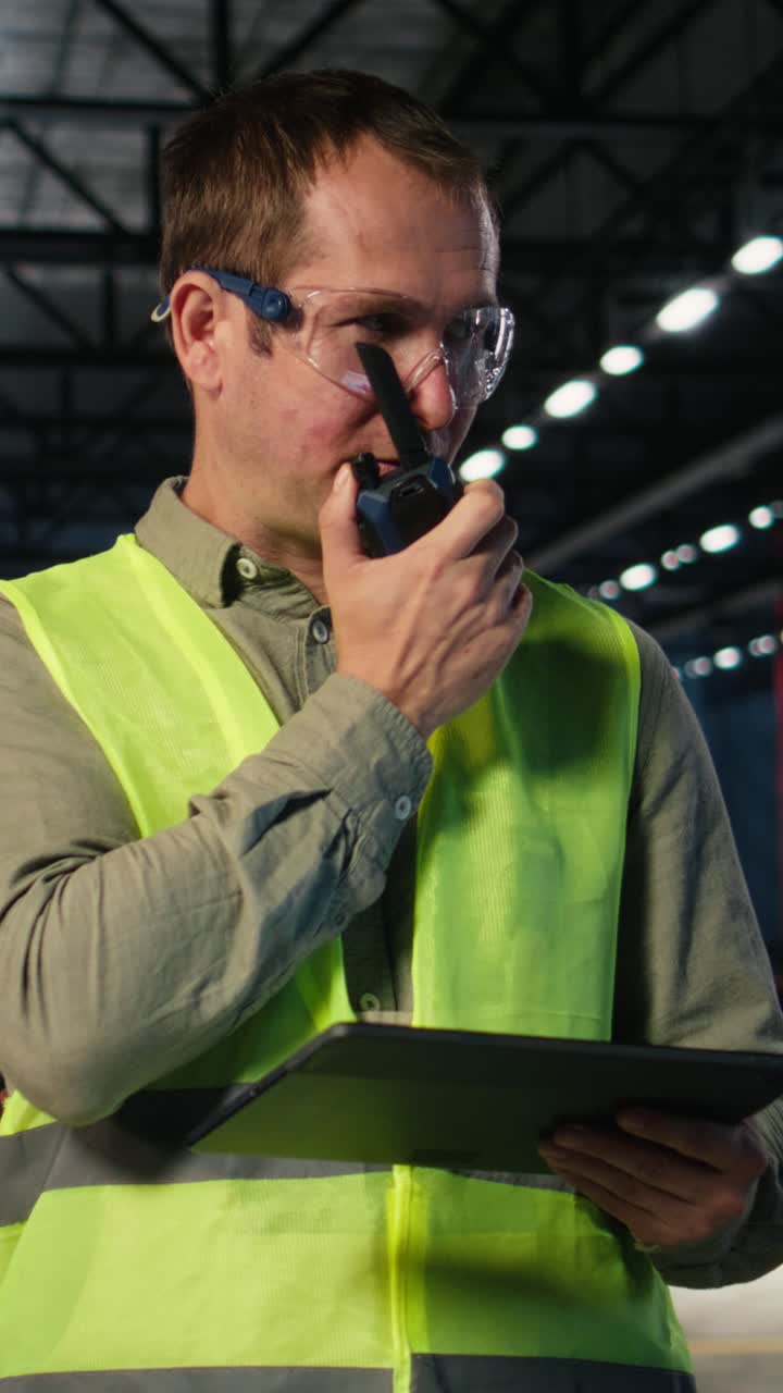 Vertical Video Industrial staff member uses walkie talkie device to coordinate assembly tasks