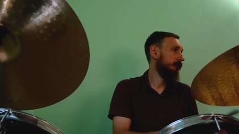 drummer warming up with drum brushes. bearded man playing rock and metal music on drums on green wall background. music band rehearsal jamming 4k footage.