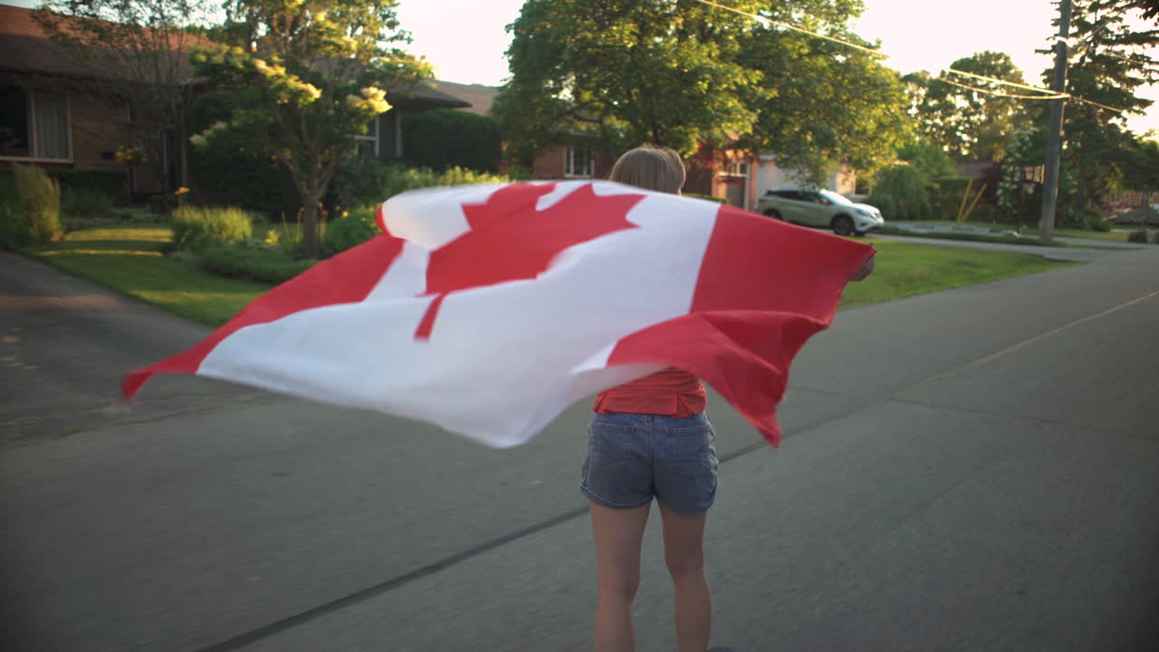 Ragazza in longboard che sventola una bandiera canadese dietro di sé all'ora d'oro.