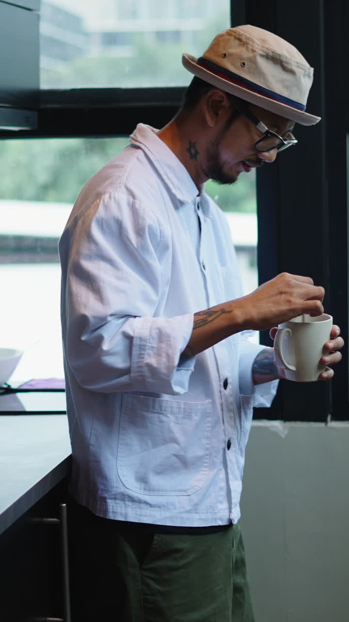 Uomo con cappello e occhiali con tazza in cucina