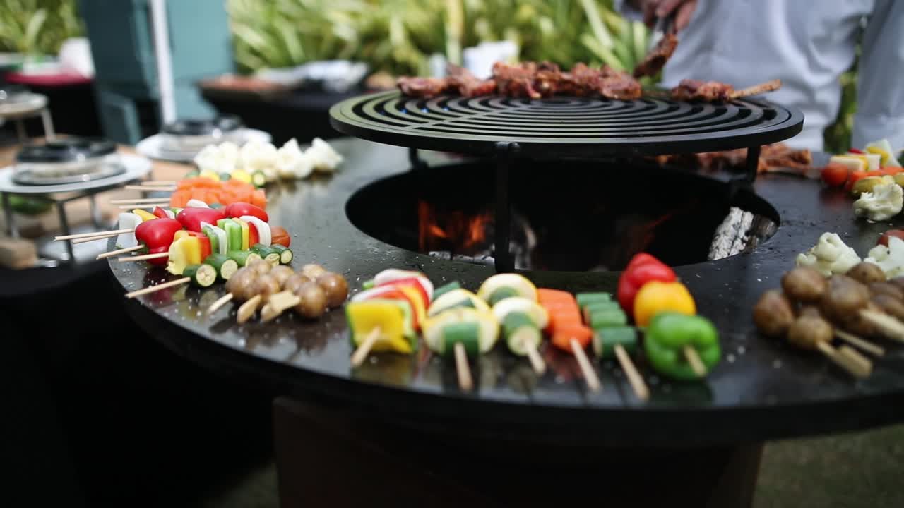 Chef putting meat on round grill with vegetables