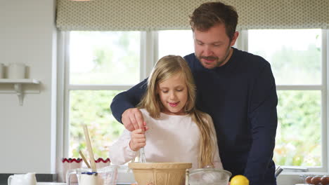father and daughter wearing pyjamas making baking in kitchen at home together