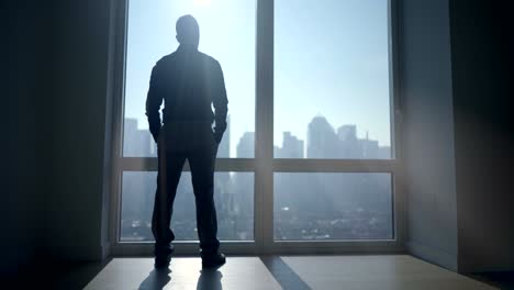 outlines of man opening blinds on big windows. sun shines into the room, producing shadows.