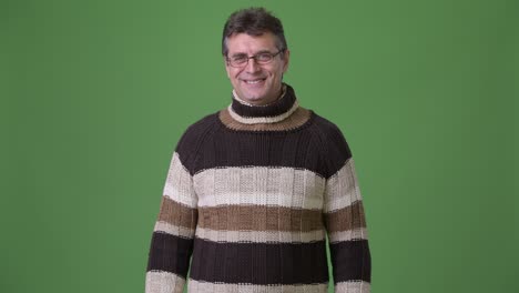 mature handsome man wearing turtleneck sweater against green background