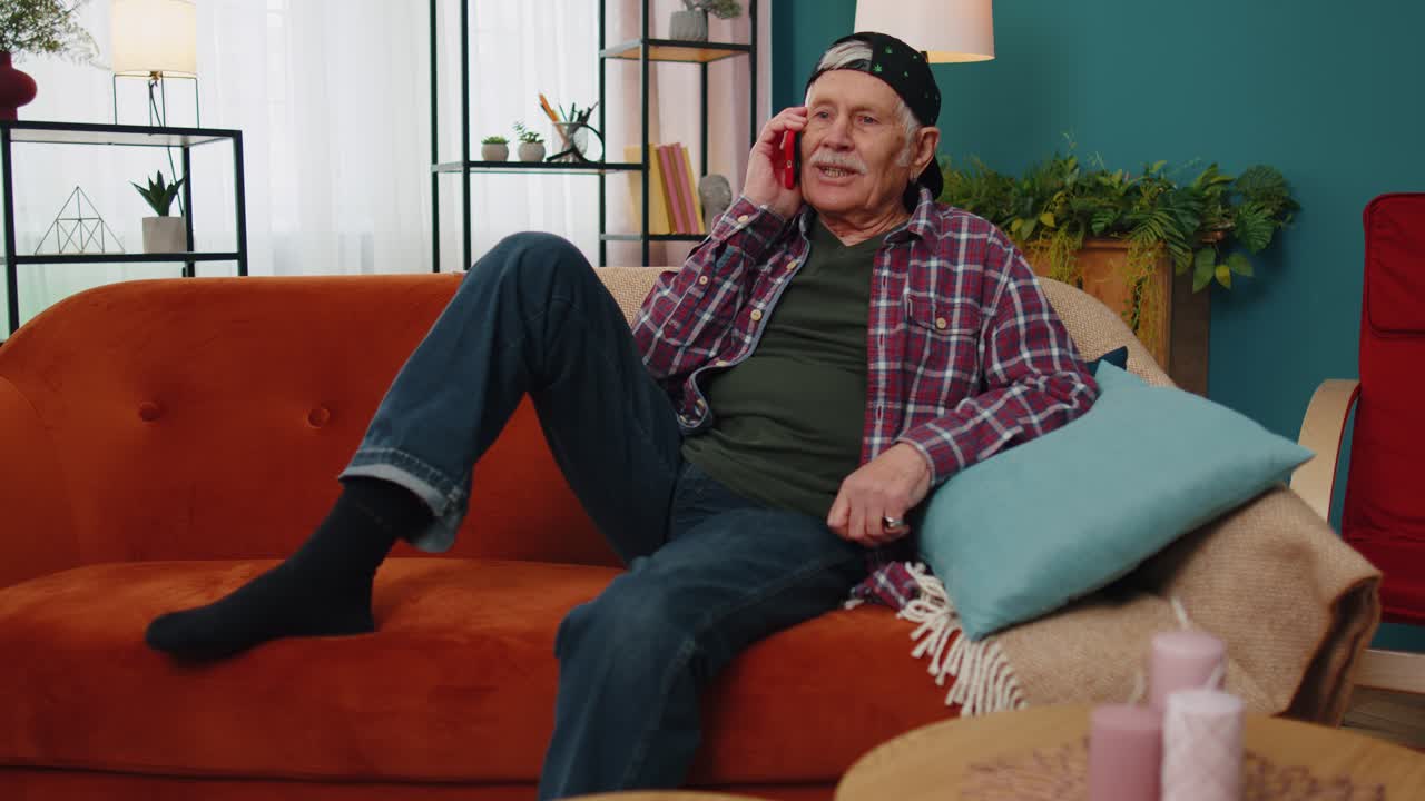 Happy stylish senior grandfather man holding smartphone talking with friends at home conversation