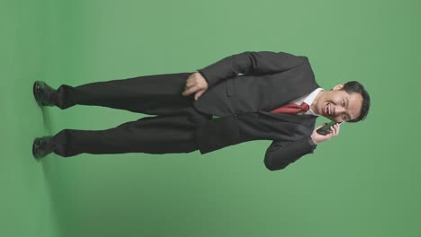 full body of smiling asian business man talking on mobile phone on green screen in the studio