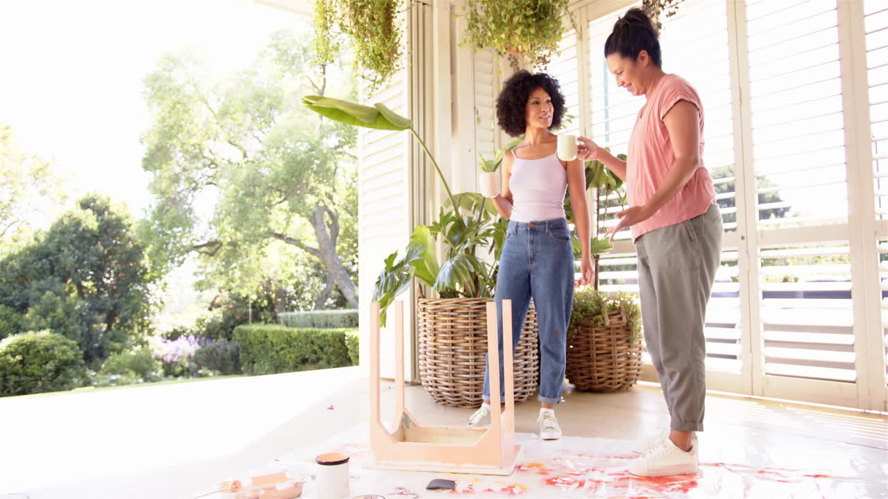 Painting wooden furniture, mother and adult daughter enjoying DIY project on porch with plants
