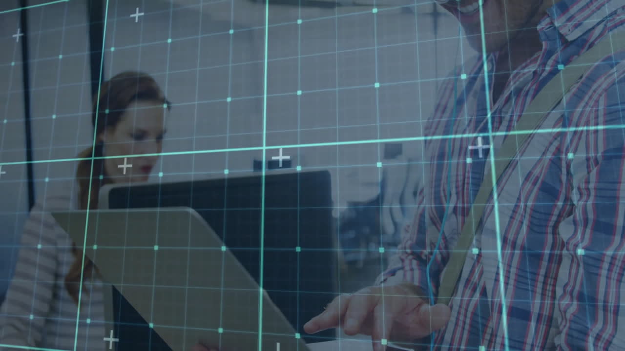 Female coworker typing on laptop beside male coworker in tech office, showcasing data grid overlay