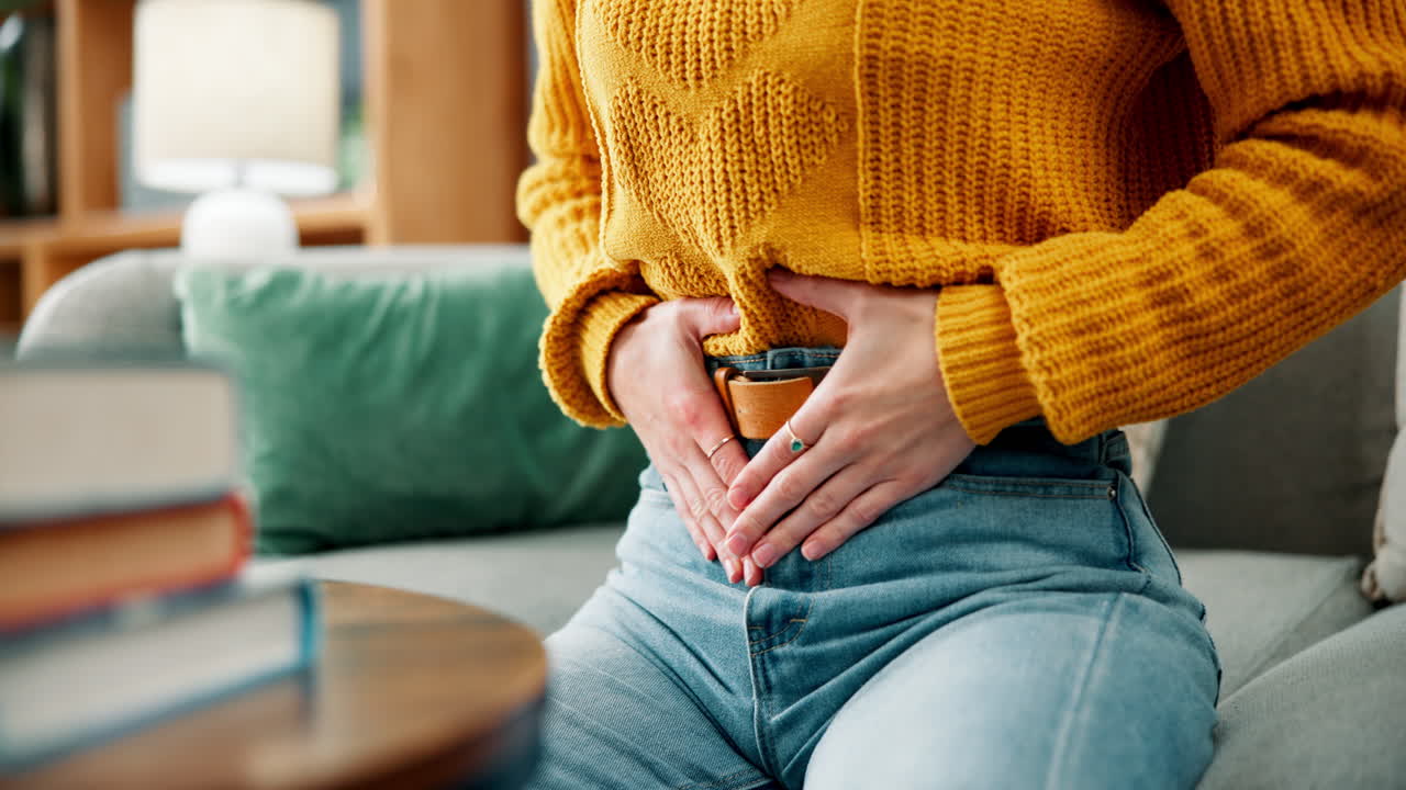 Woman experiencing abdominal pain while sitting on the sofa