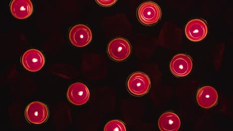 overhead shot of romantic lit red candles on background covered in rose petals