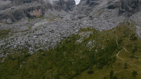 Stunning-birds-eye-shot-of-forest-trees-and-rocks-between-mountain-range-during-cloudy-day---aerial-tilt-up