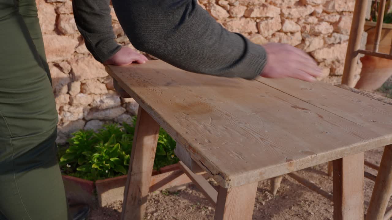 un hombre preparando una mesa de madera para una comida, a principios de la primavera en el campo en una antigua casa de piedra entre olivos mediterráneos