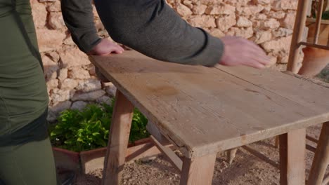 Un-Hombre-Preparando-Una-Mesa-De-Madera-Para-Una-Comida,-A-Principios-De-La-Primavera-En-El-Campo-En-Una-Antigua-Casa-De-Piedra-Entre-Olivos-Mediterráneos