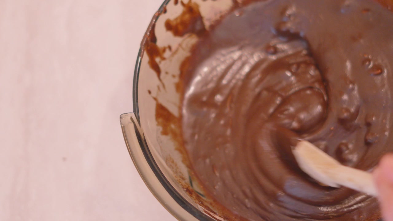 Mescolando preparato per torta brownie al cioccolato in una ciotola di vetro con spazio per testo a lato. Riprese di pasticceria casalinga.