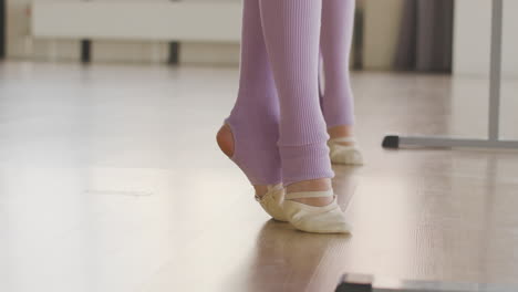 camera focuses on the feet of gymnastic girls in ballet shoes and socks rehearsing a ballet move