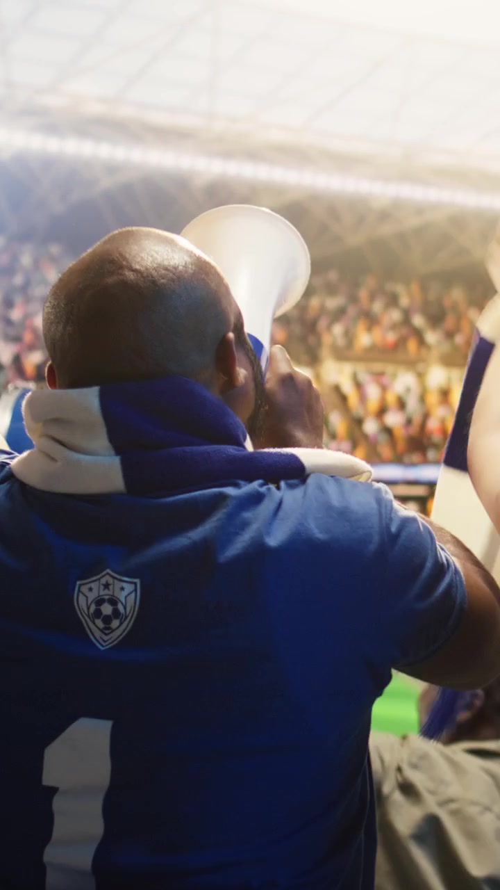 Video verticale: Tifosi di calcio con maglie blu che suonano trombe e un megafono nello stadio