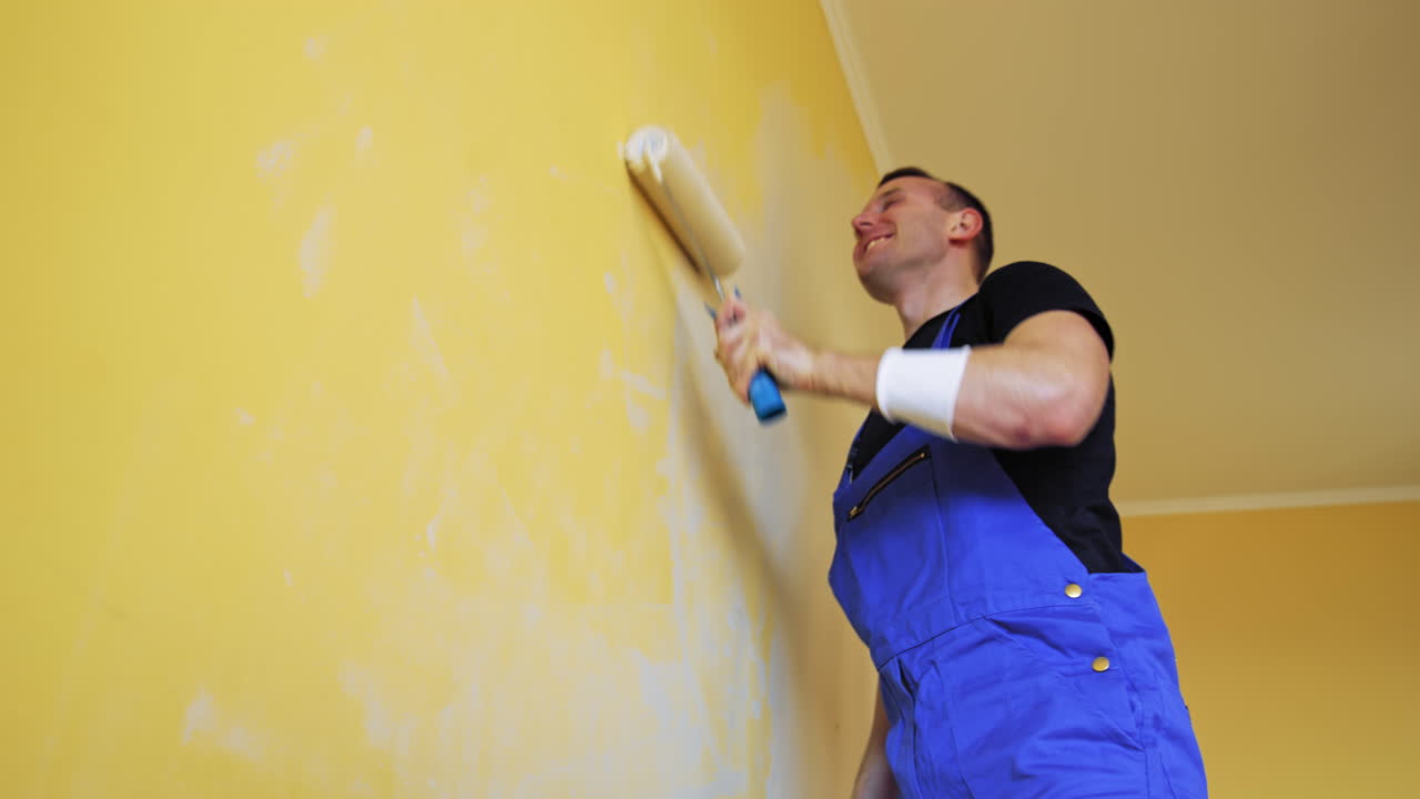 Man singing in paint brush. Cheerful man with rollers for painting the walls singing