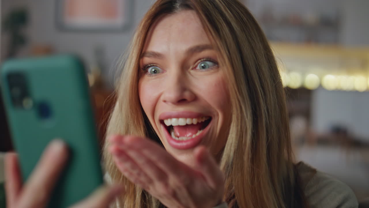 Ritratto di donna emotiva che parla in videochiamata sullo smartphone, seduta in soggiorno.