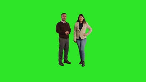 full length studio portrait of smiling male and female teachers or businesspeople standing against green screen background