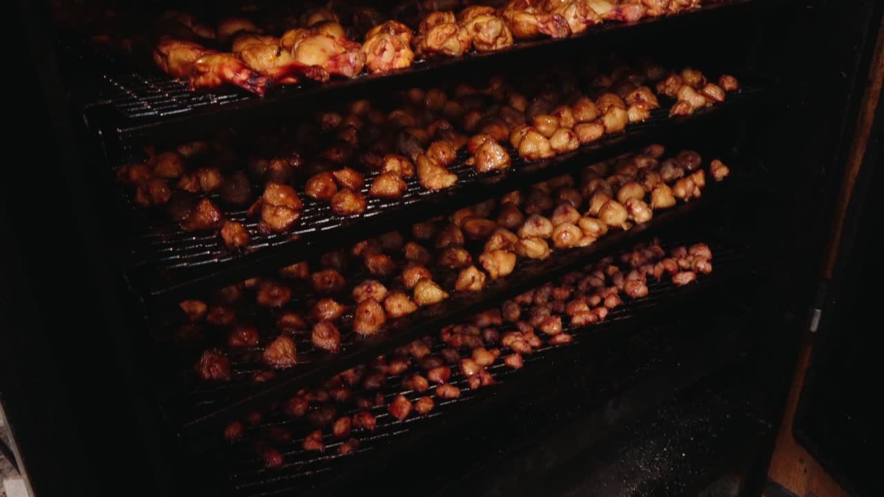 Various types of fish, including eel and redfish, are being smoked on a grill rack. The golden-brown color and rich texture highlight the traditional smoking process.