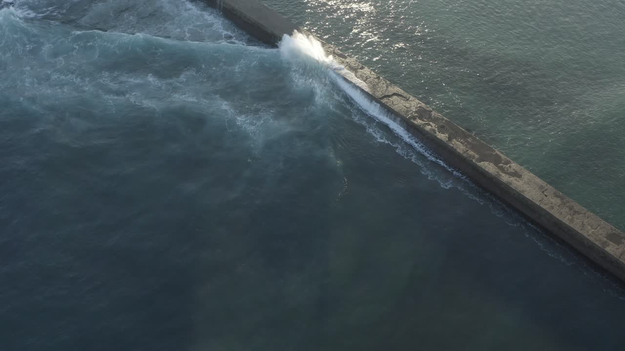 Waves crashing on breakwater. Aerial top-down forward