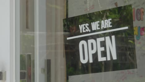 close-up of yes we are open sign on transparent glass shop door inviting customers