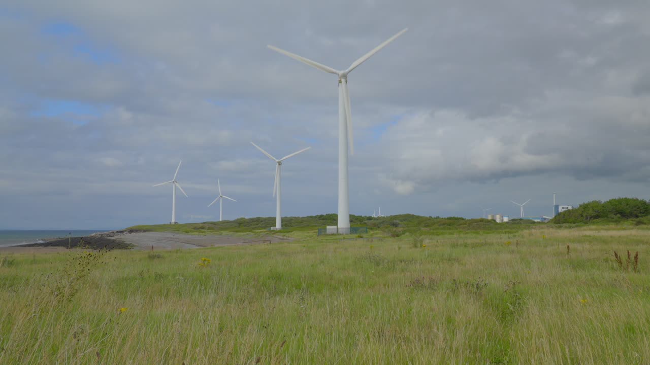노란색 풀을 통해 회전하는 풍차는 구름이 많은 여름 하늘을 보여주는 풀을 고 있습니다.